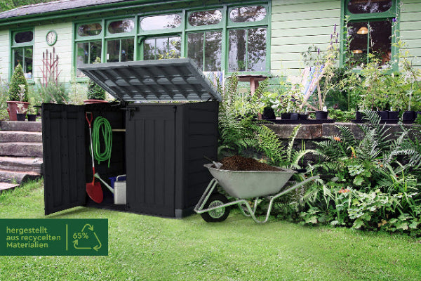 Vista en bonito jardín con el cobertizo Keter Store It Out MAX de 1200 litros con puerta y tapa abiertas y artículos de jardinería