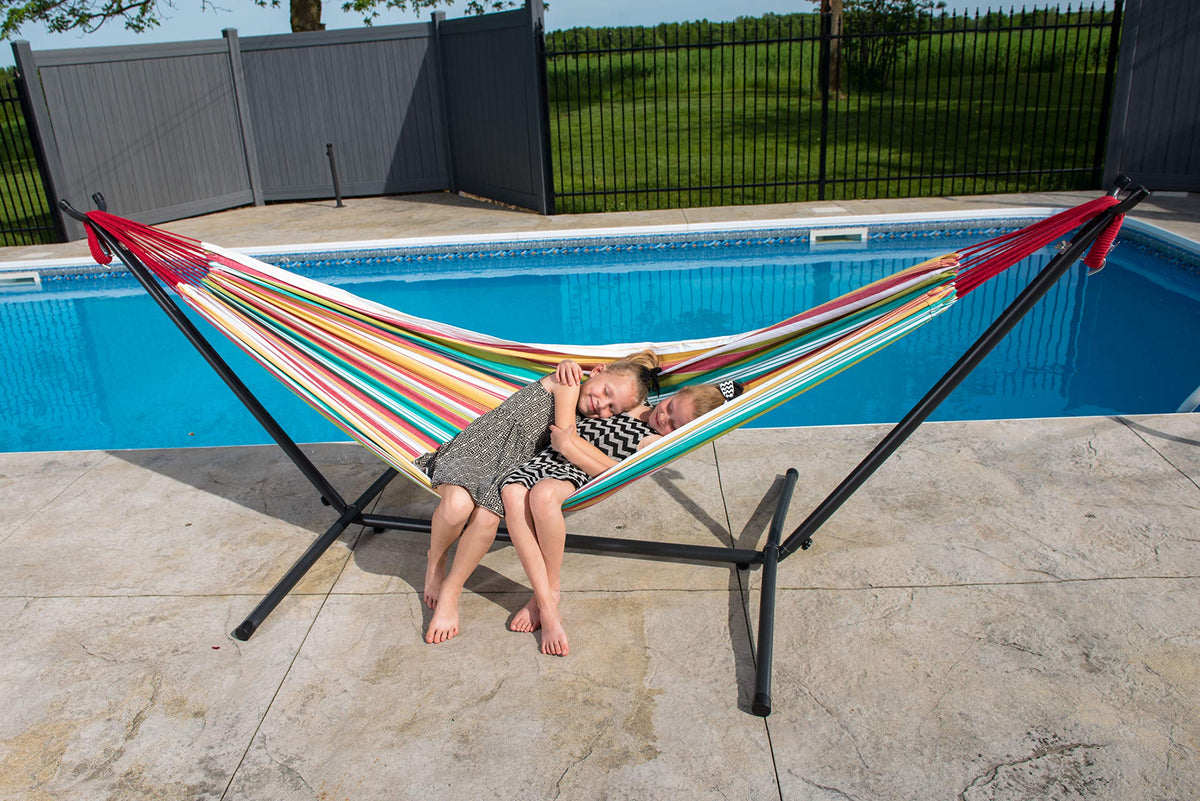 Niñas descansando en hamaca Vivere a rayas de colores con estructura junto a piscina