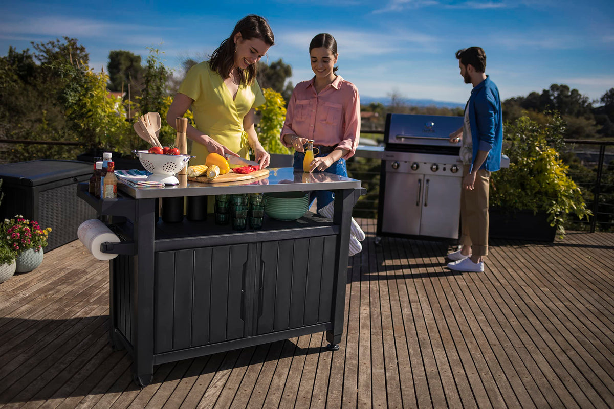 Vista en bonita terraza de amigos cocinando con el Mueble auxiliar para Barbacoa grande para jardín, Color marrón. Unity XL de Keter