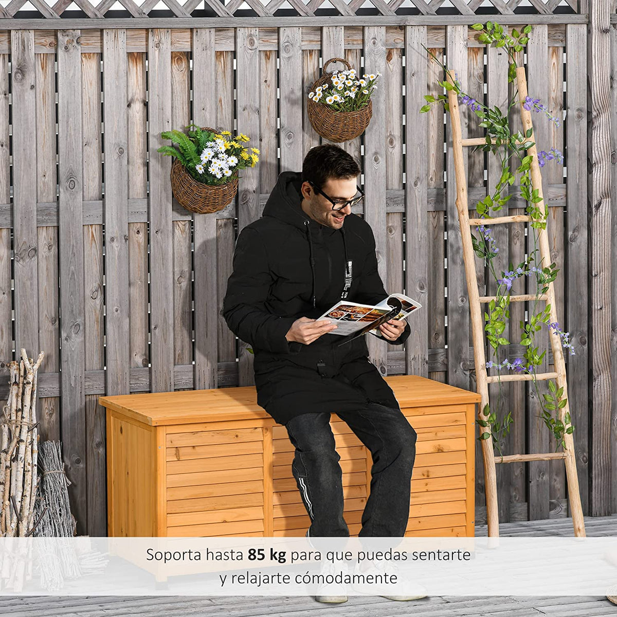 Hombre en patio exterior sentado sobre la Caja de Almacenamiento de Madera para Exterior con Tapa y Diseño tipo Persiana 127x56x60 cm Color natural. Vista general con tapa abierta. Outsunny